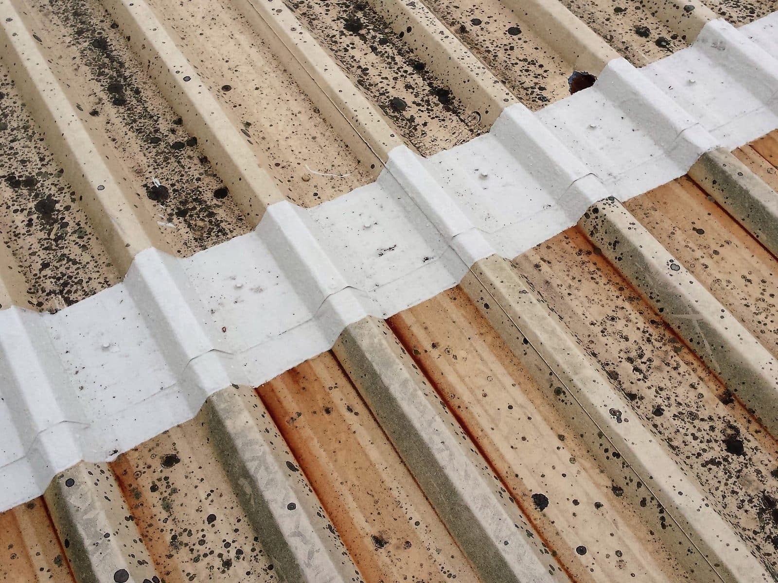 A white coated end lap on a moss-speckled profiled roof, rust streaks running down the sheets below it