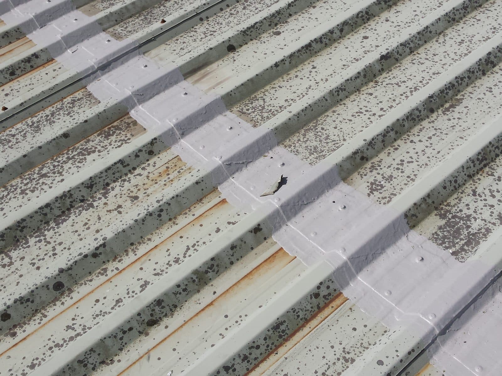 A grey coated band across an end lap on a moss-speckled profiled roof, rust lines still showing beneath it